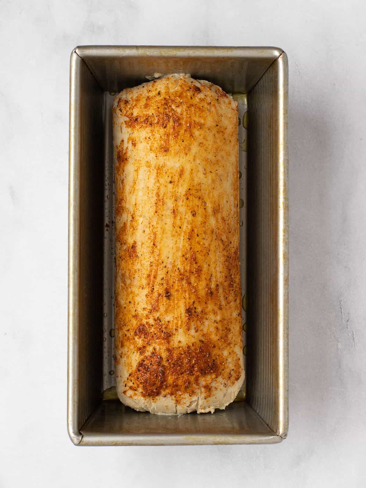 Gefilte fish loaf in a baking pan brushed with oil and spices.