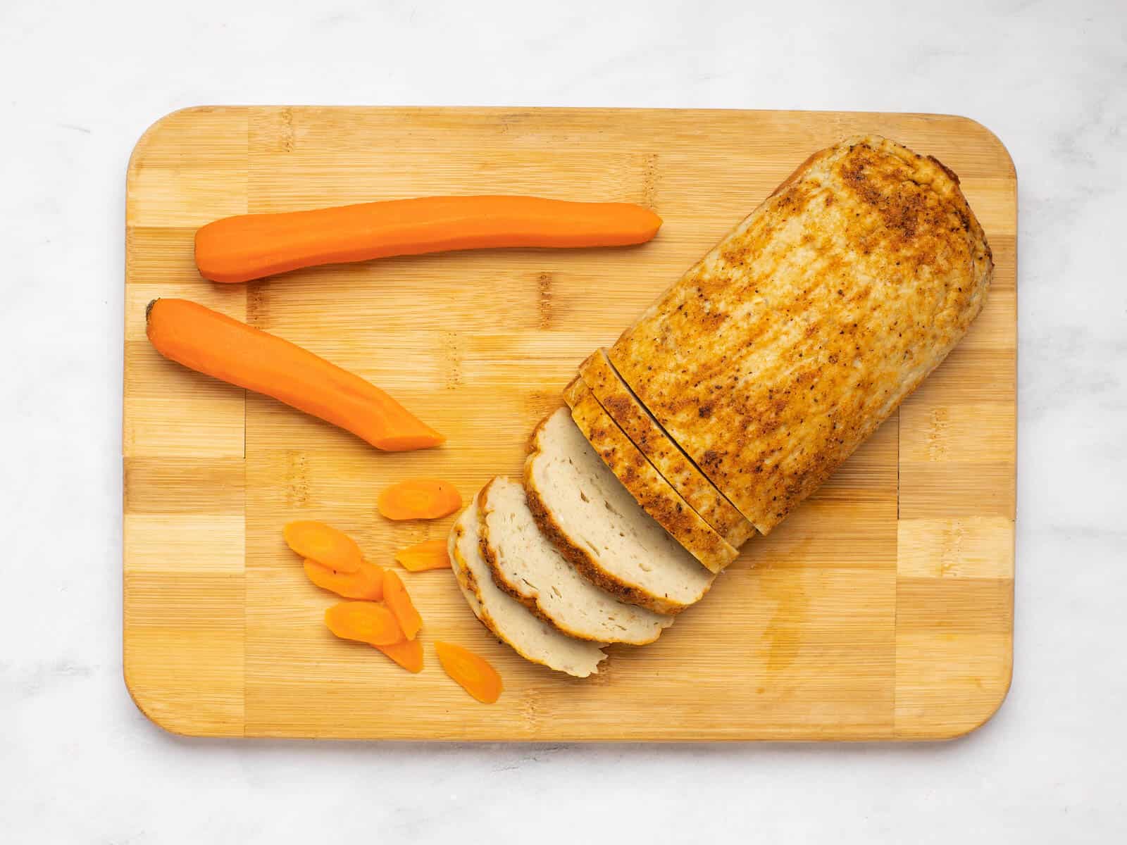 Sliced baked gefilte fish on a cutting board with carrots.