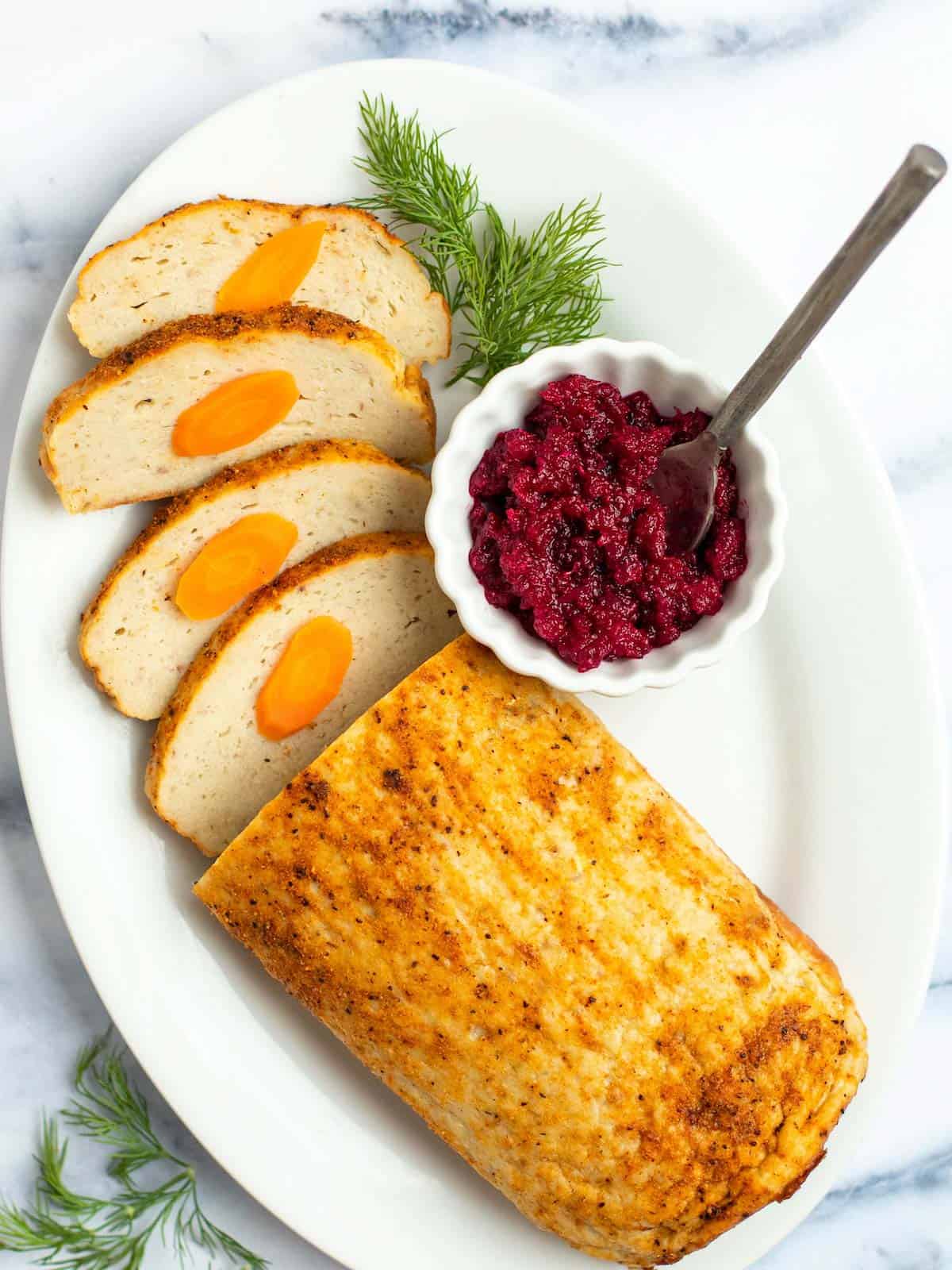 Sliced baked gefilte fish loaf on a serving platter with beet horseradish and dill.