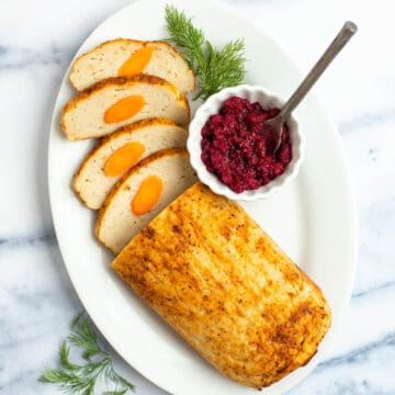 Sliced baked gefilte fish loaf on a serving platter with beet horseradish.