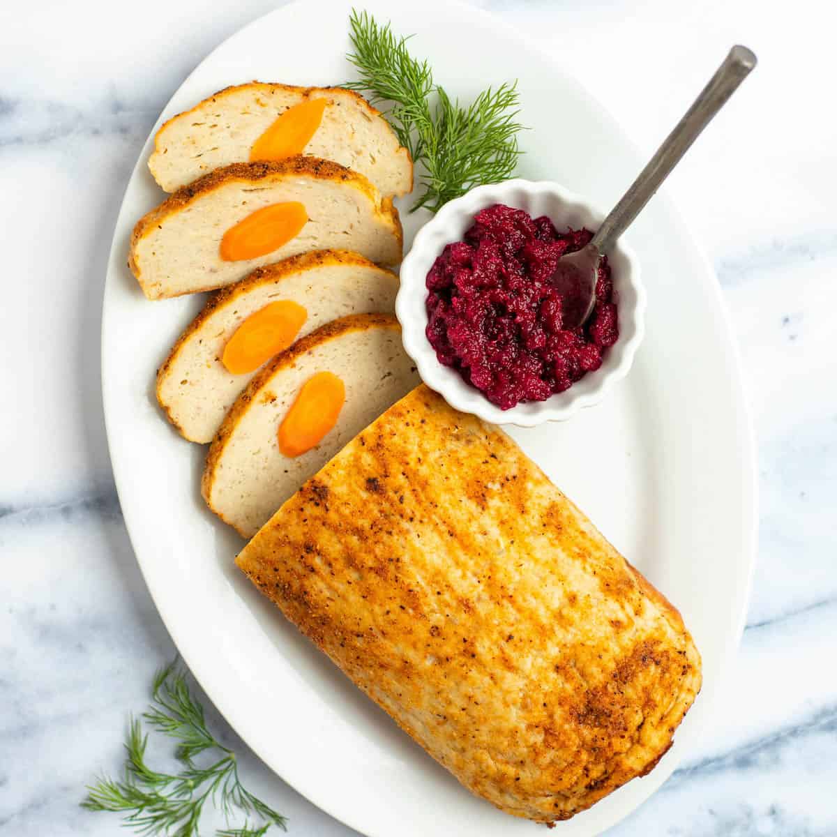 Sliced baked gefilte fish loaf on a serving platter with beet horseradish.