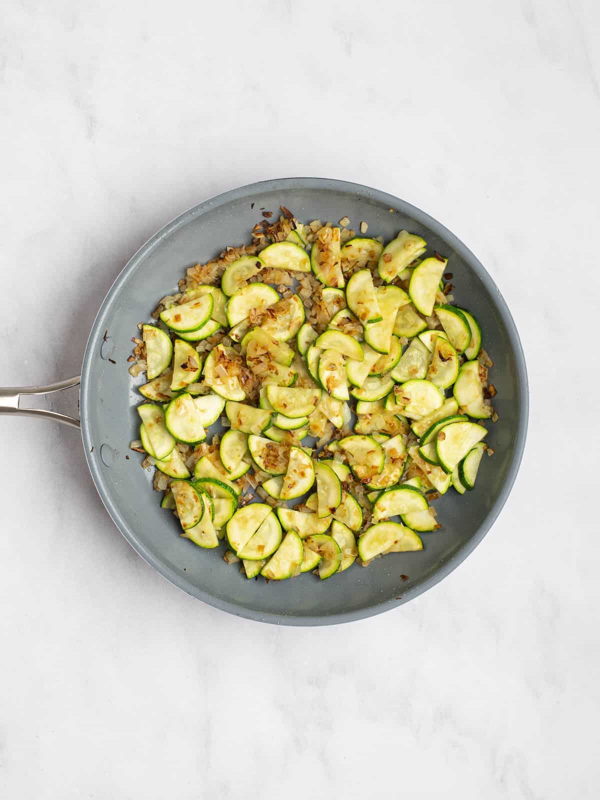 A skillet with sautéed onions and sliced zucchini.