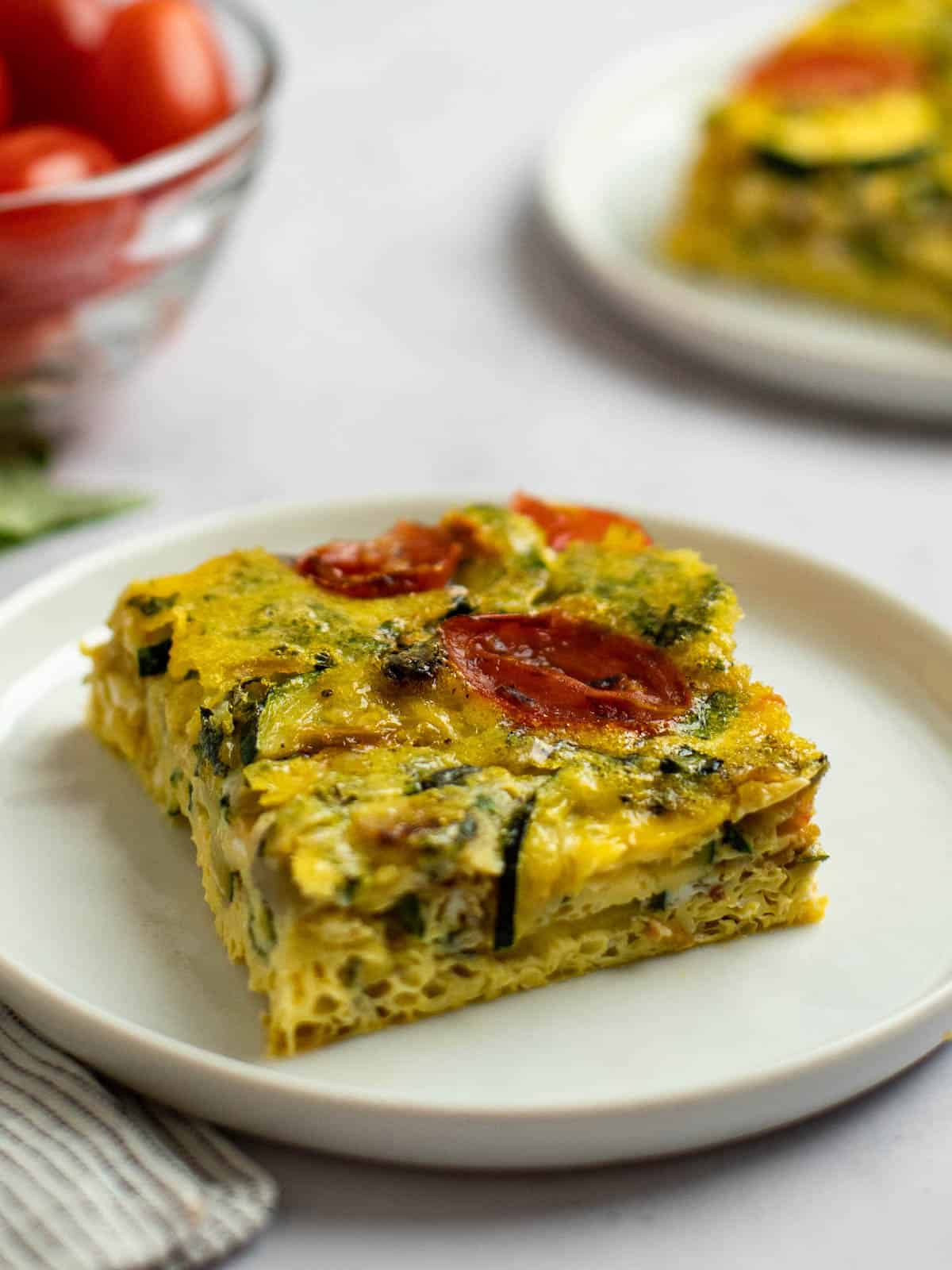 A sliced square of baked Italian frittata with tomatoes and zucchini.