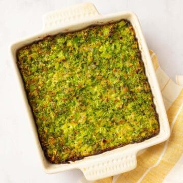 Golden brown broccoli kugel in a white baking dish with yellow towel.