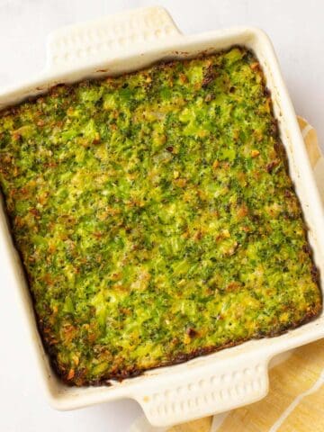 Golden brown broccoli kugel in a white baking dish with yellow towel.