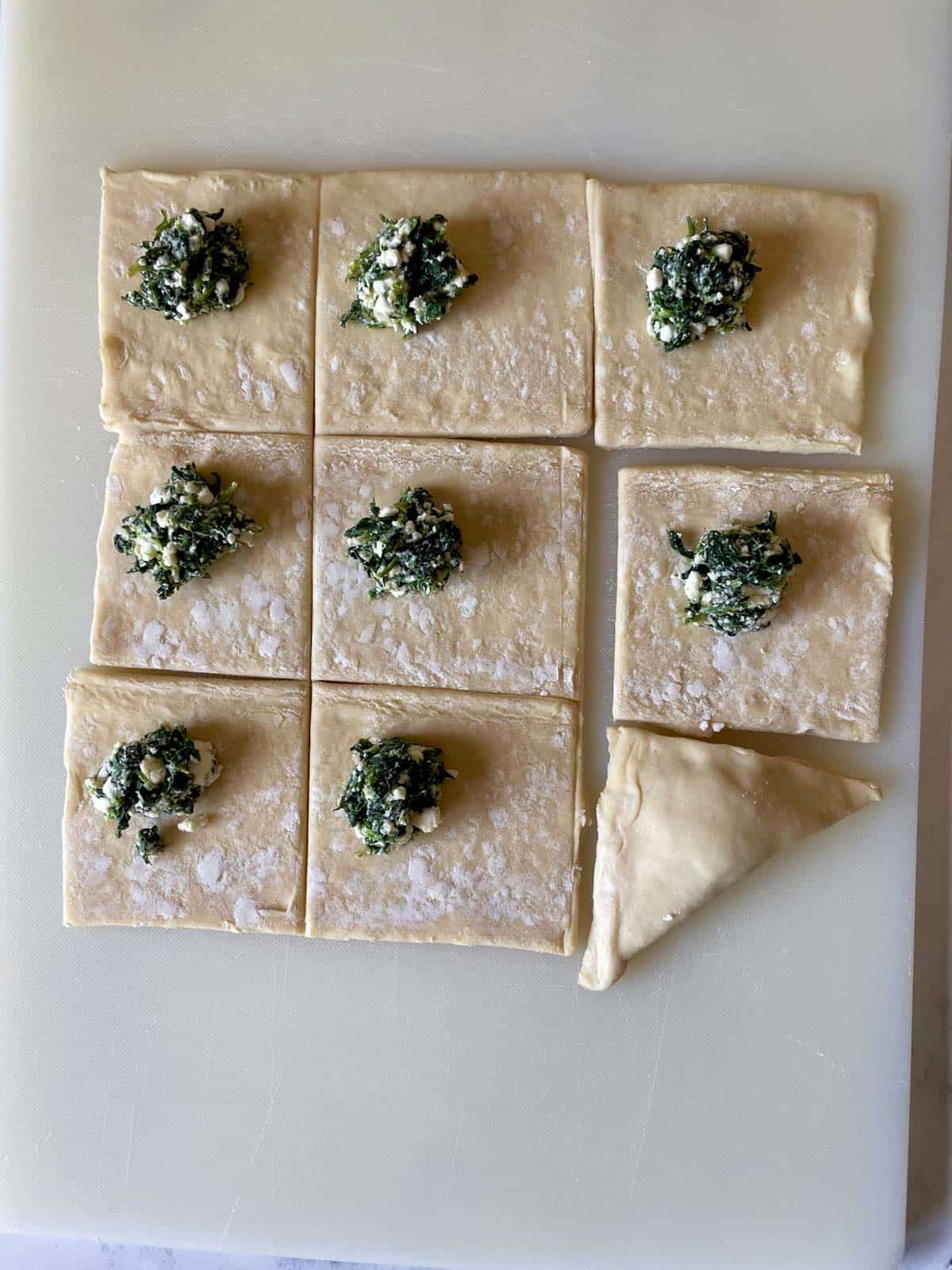 Puff pastry dough cut into squares with a teaspoon of spinach and feta filling.