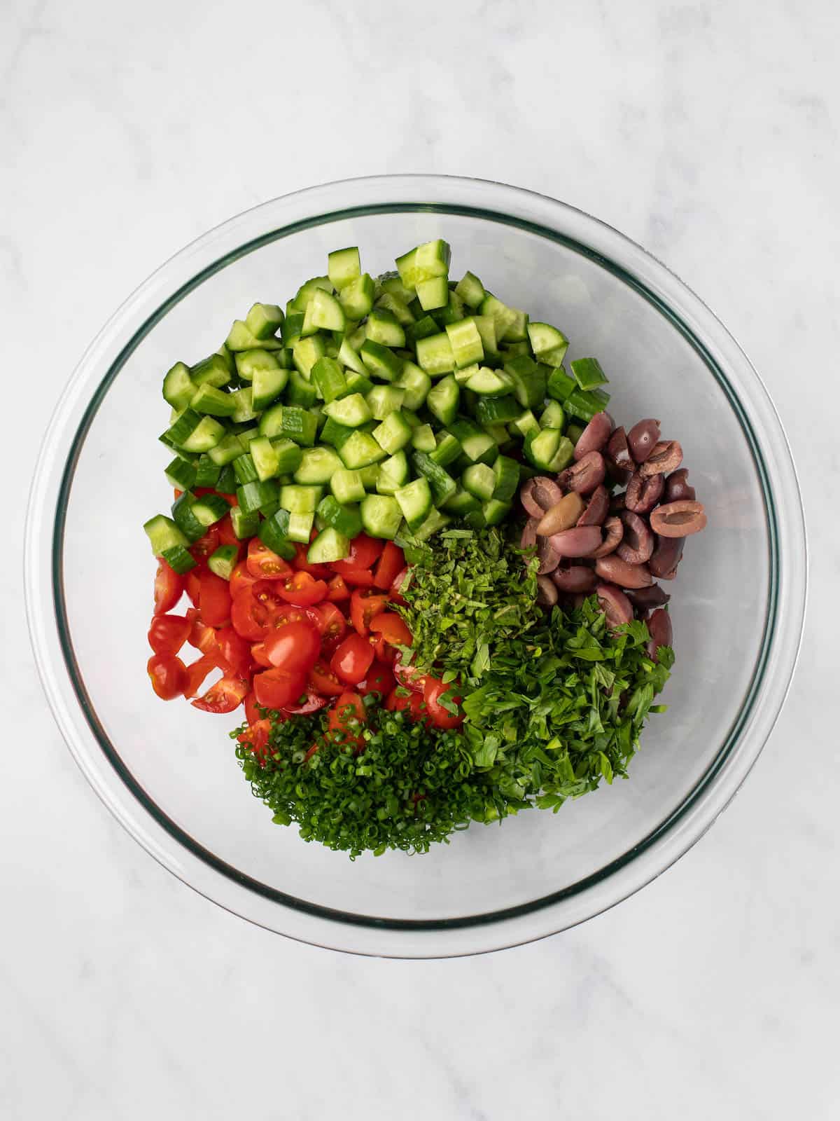 Chopped cucumber, tomato, olives, and fresh herbs in a bowl.