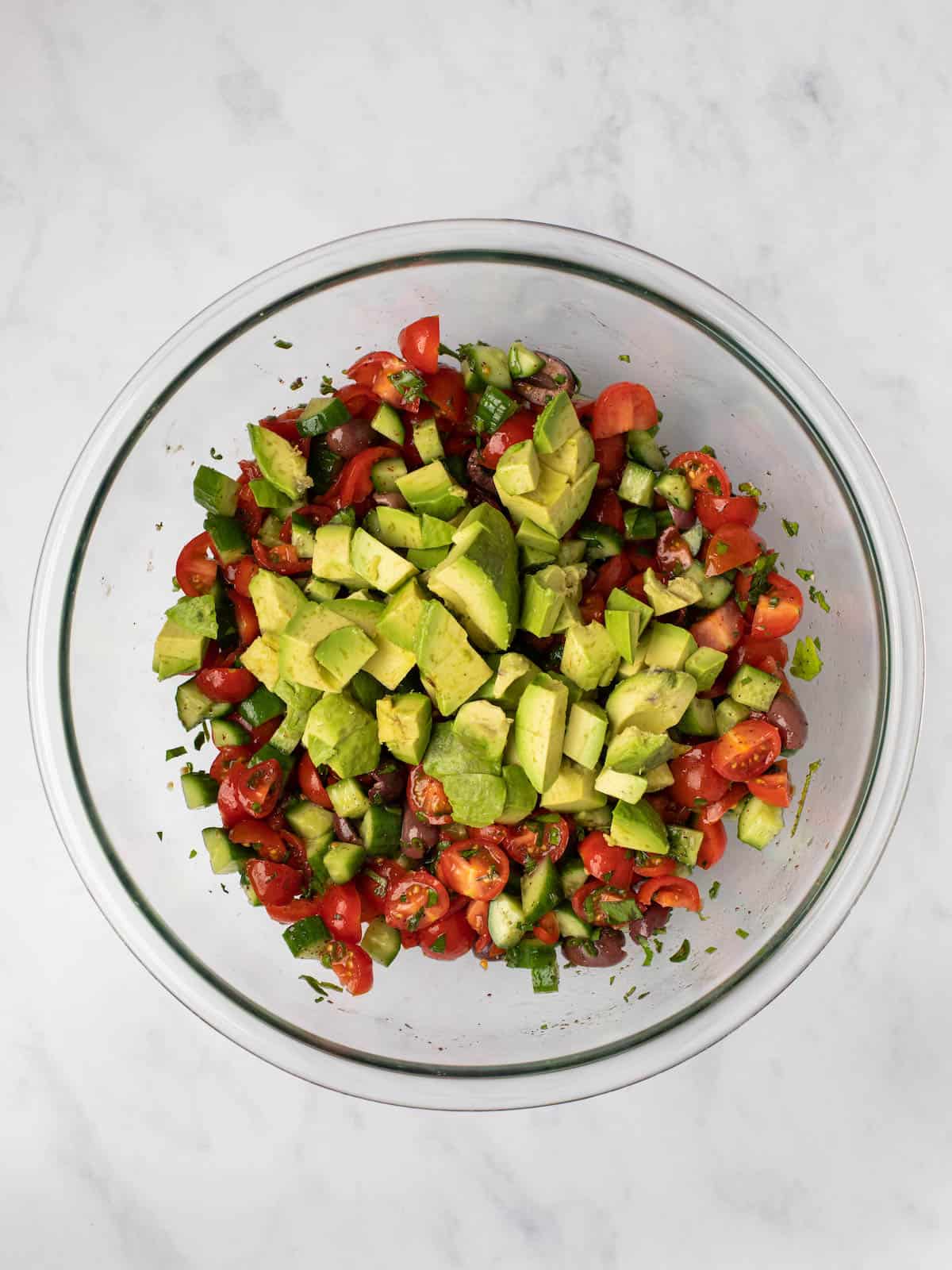Adding diced avocado to a chopped cucumber and tomato salad.
