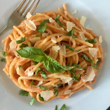 Spaghetti with fresh tomato sauce garnished with parmesan and basil on a white plate.