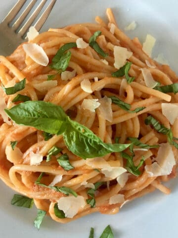 Spaghetti with fresh tomato sauce garnished with parmesan and basil on a white plate.