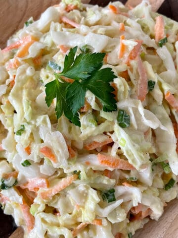 A bowl of coleslaw with cabbage, carrots, and green onions.