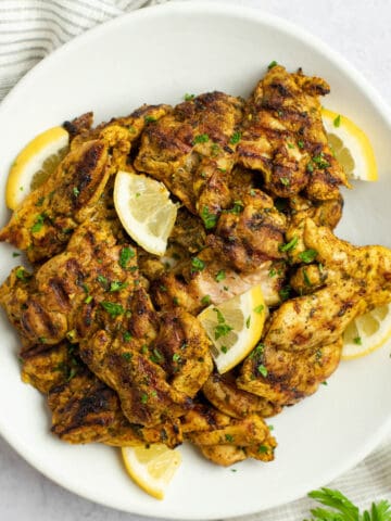 Pargiot grilled chicken thighs with Israeli spices on a plate with parsley and lemon.