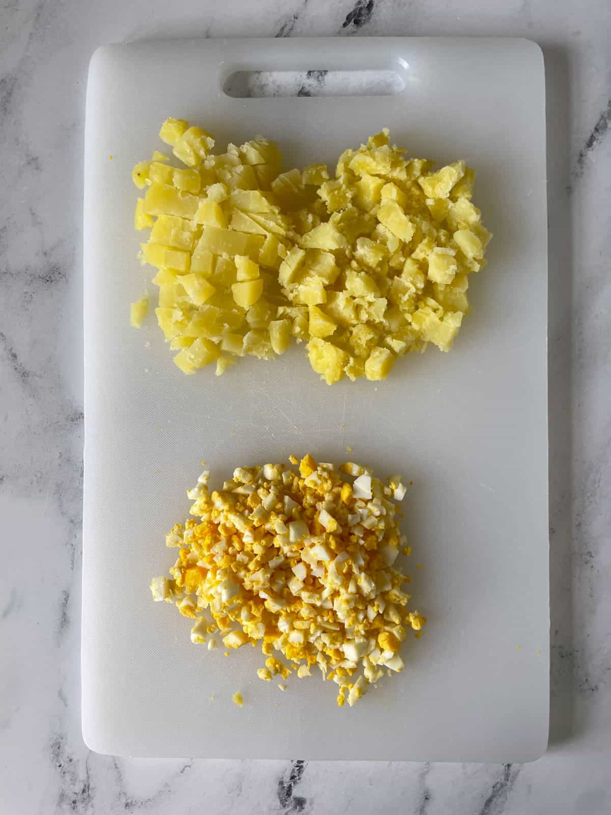 Chopped potatoes and eggs for potato salad on a cutting board. 