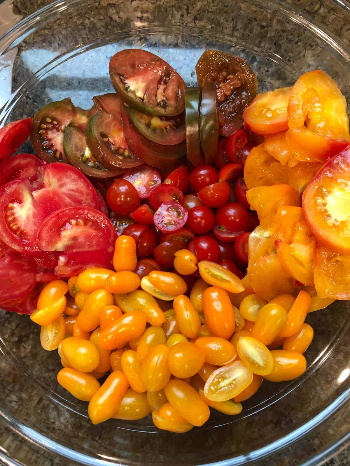 Sliced tomatoes of different varieties in a glass mixing bowl.