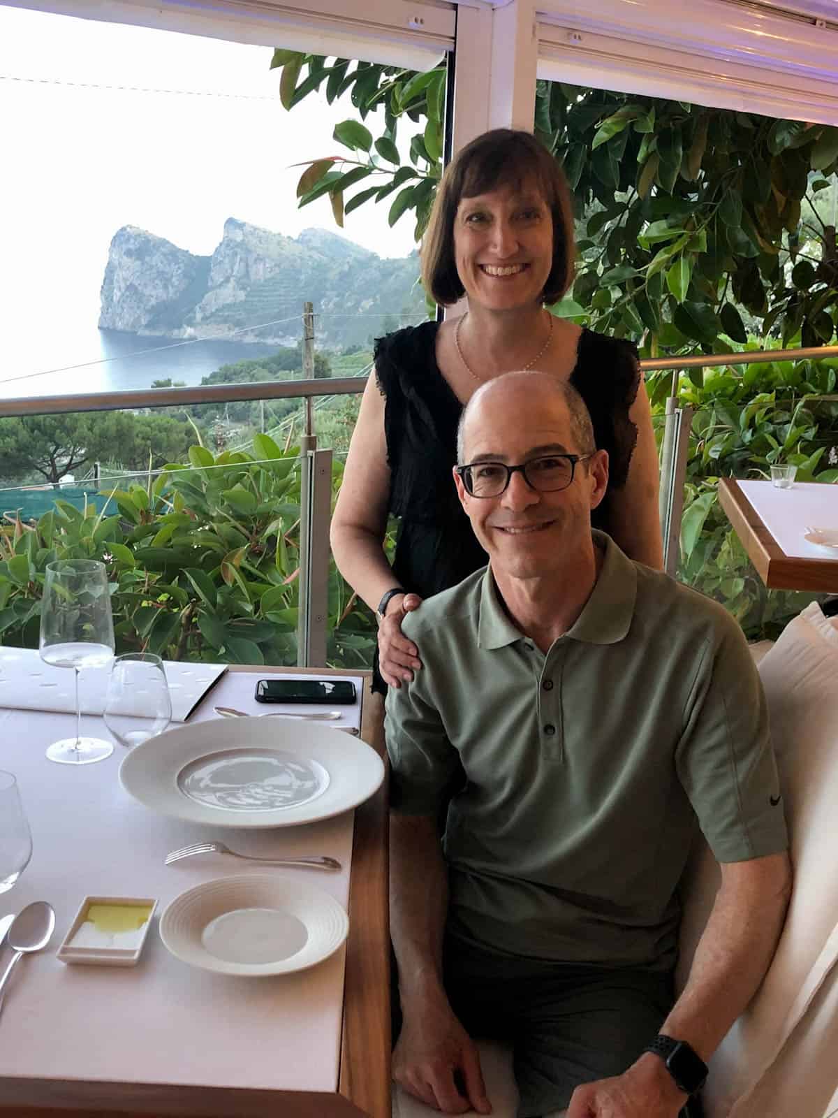 Dana and her husband at a restaurant table overlooking the Bay of Nerano in Italy.