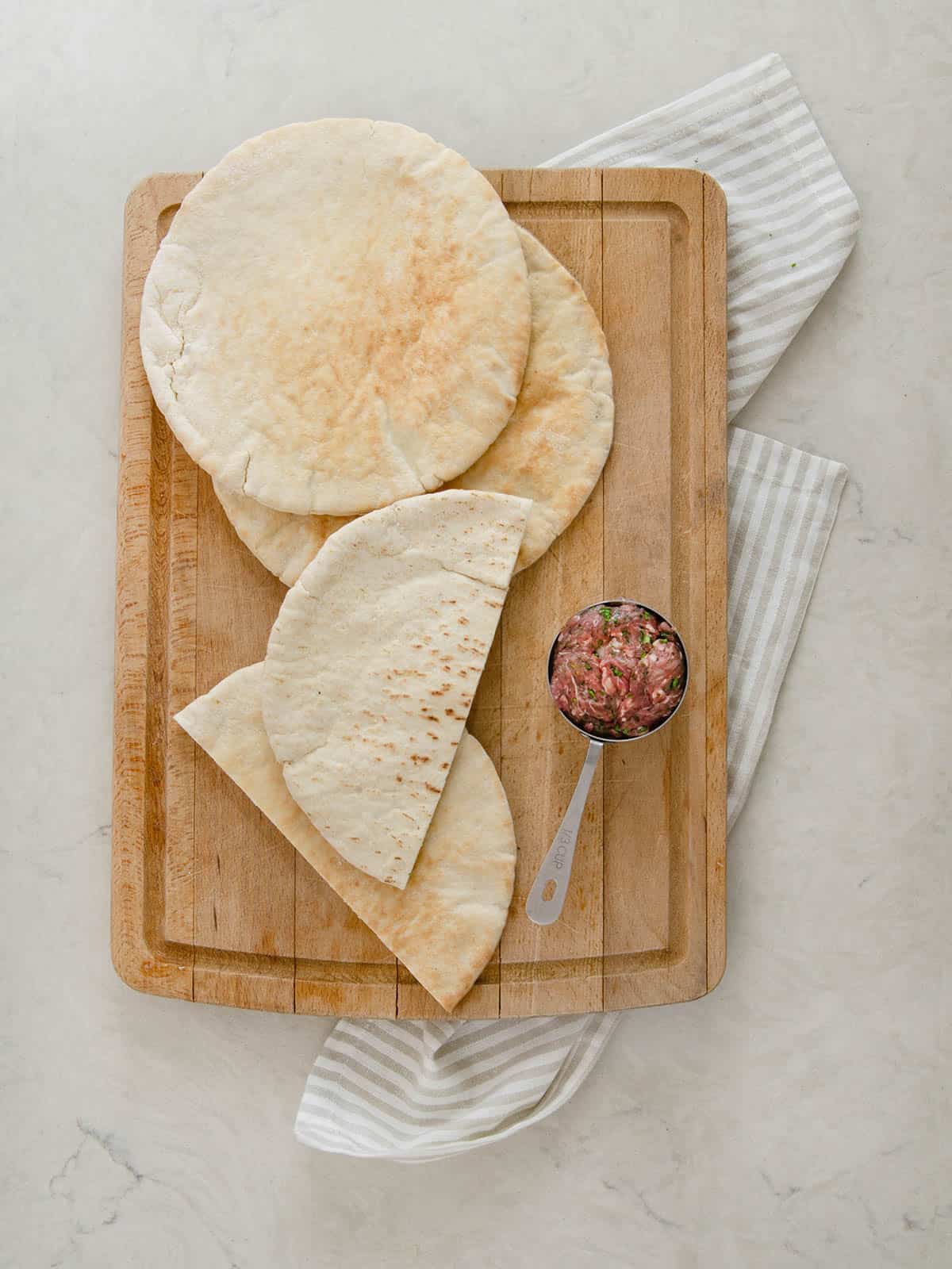 Pita bread on a cutting board with a scoop of ground meat mixture.