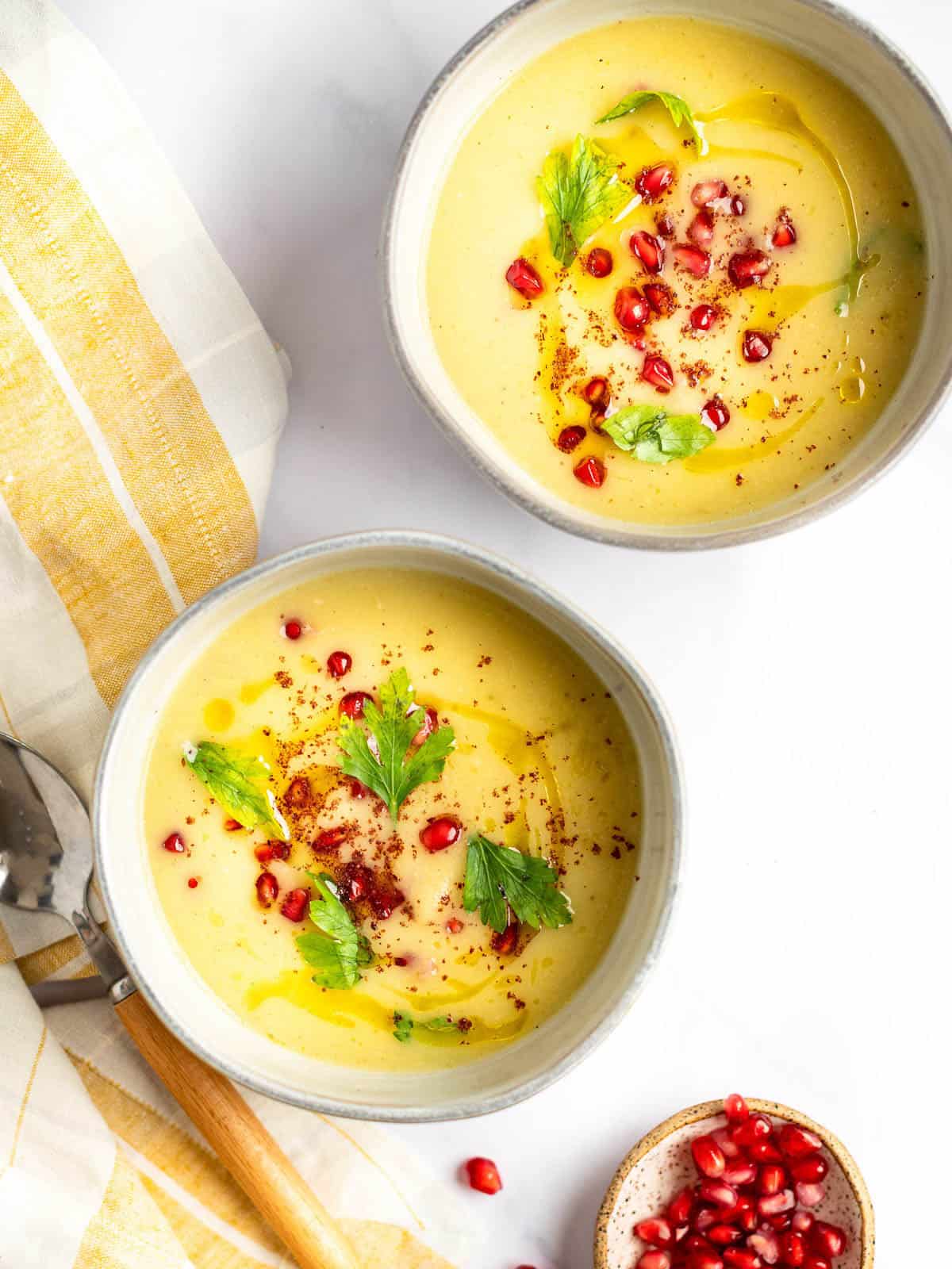 Two bowls of parsnip and apple soup topped with pomegranate seeds.