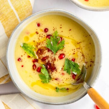 Parsnip and apple soup in a bowl topped with parsley and pomegranate seeds.