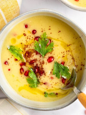Parsnip and apple soup in a bowl topped with parsley and pomegranate seeds.