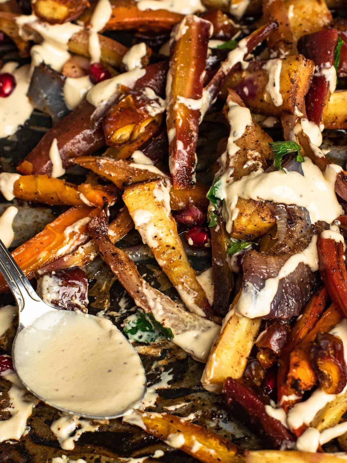 Roasted tzimmes with carrots and parsnips topped with tahini drizzle and pomegranate seeds.