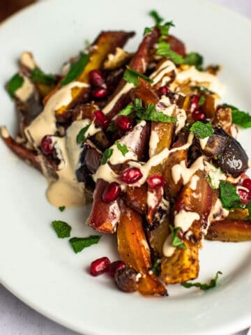 Roasted tzimmes on a plate topped with tahini drizzle, fresh mint, and pomegranate seeds.