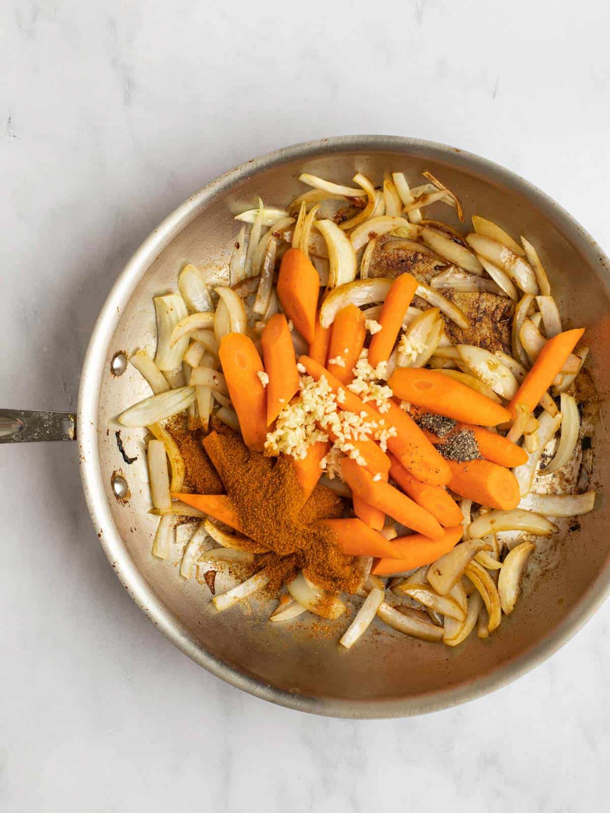 Sautéed onion in a pan with carrots, garlic, and spices.