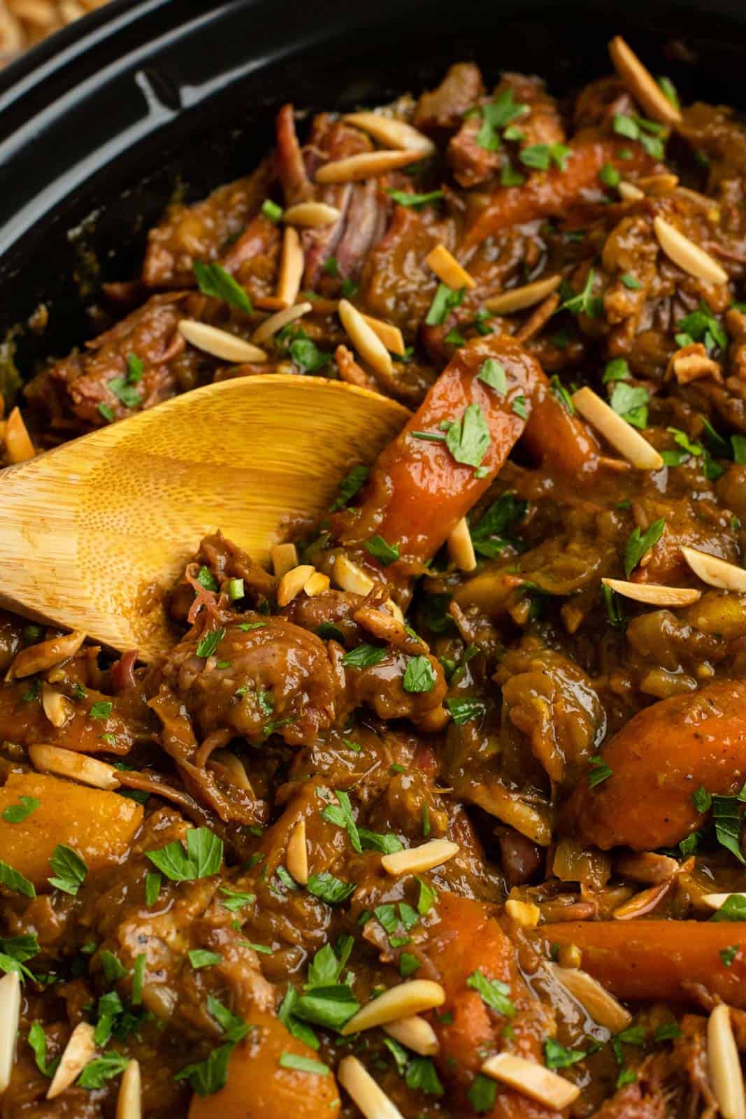 Stirring lamb tagine in a slow cooker with fresh herbs and slivered almonds.