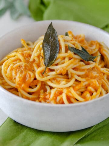 A bowl of pumpkin pasta topped with parmesan and sage.