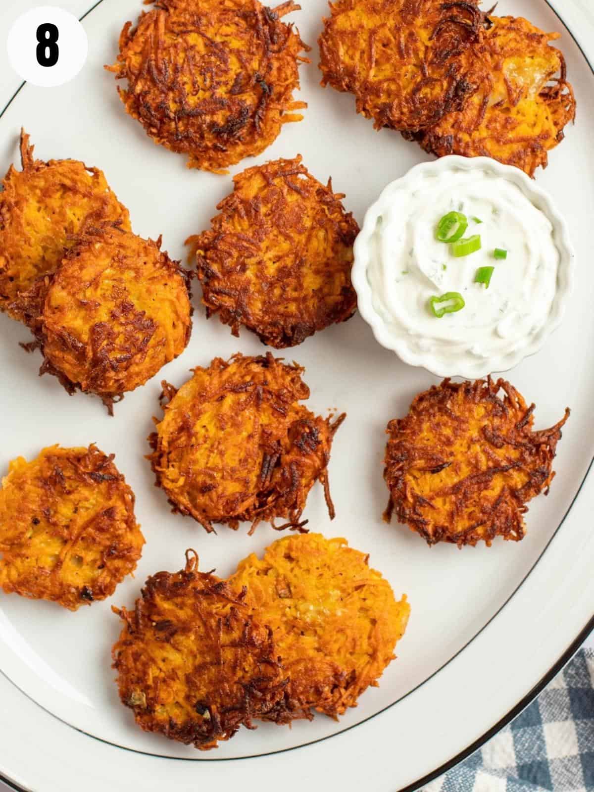 Crispy sweet potato latkes on a white plate with a dip of sour cream and chives.