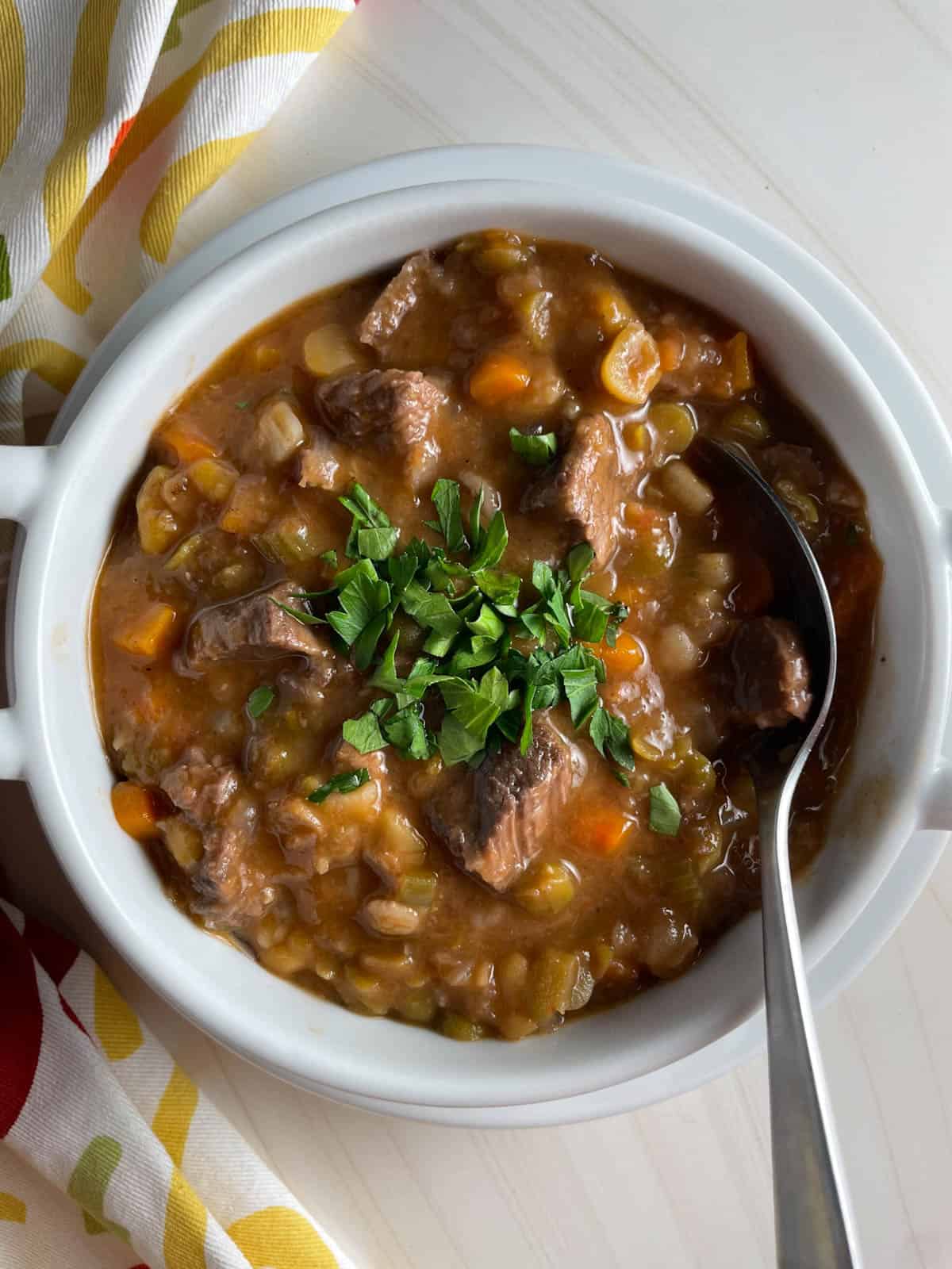 A bowl of beef barley and vegetable soup topped with fresh herbs.
