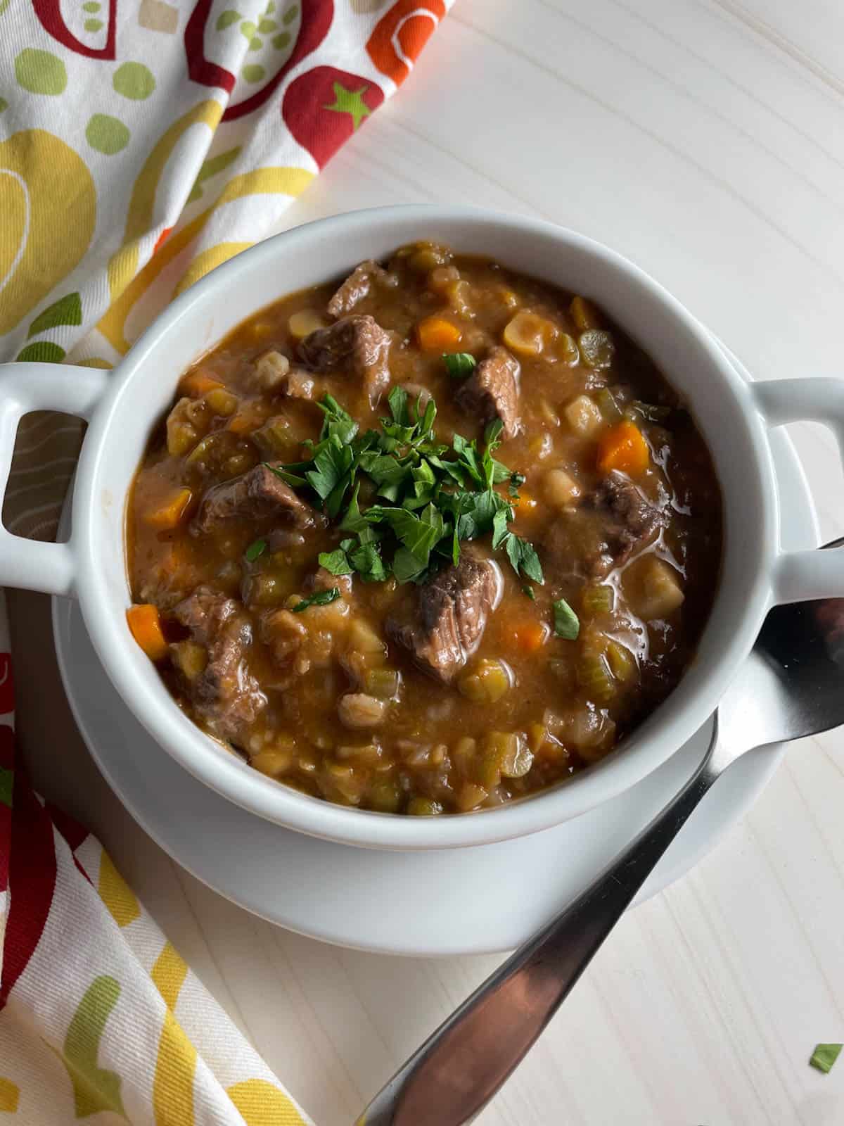 A bowl of beef barley vegetable soup topped with fresh herbs.