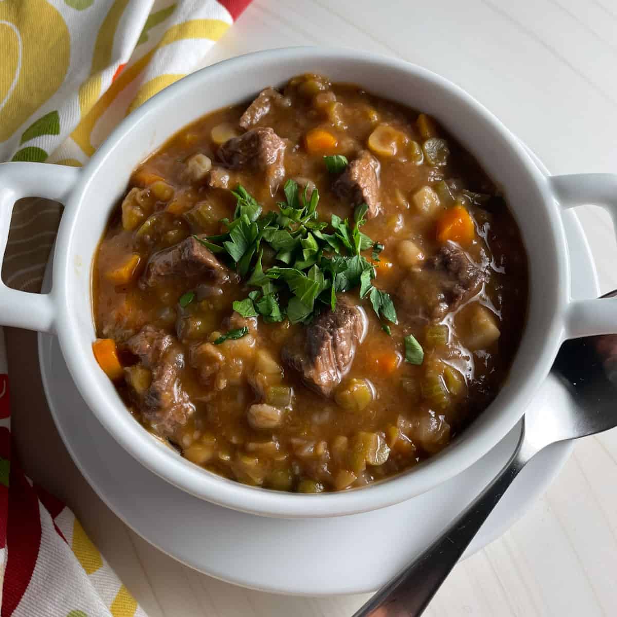 Beef barley and vegetable soup in a bowl topped with fresh herbs.