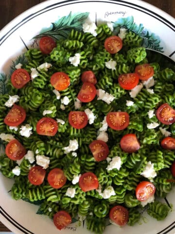 Pesto Pasta with cherry tomato and ricotta topping in a white serving bowl.