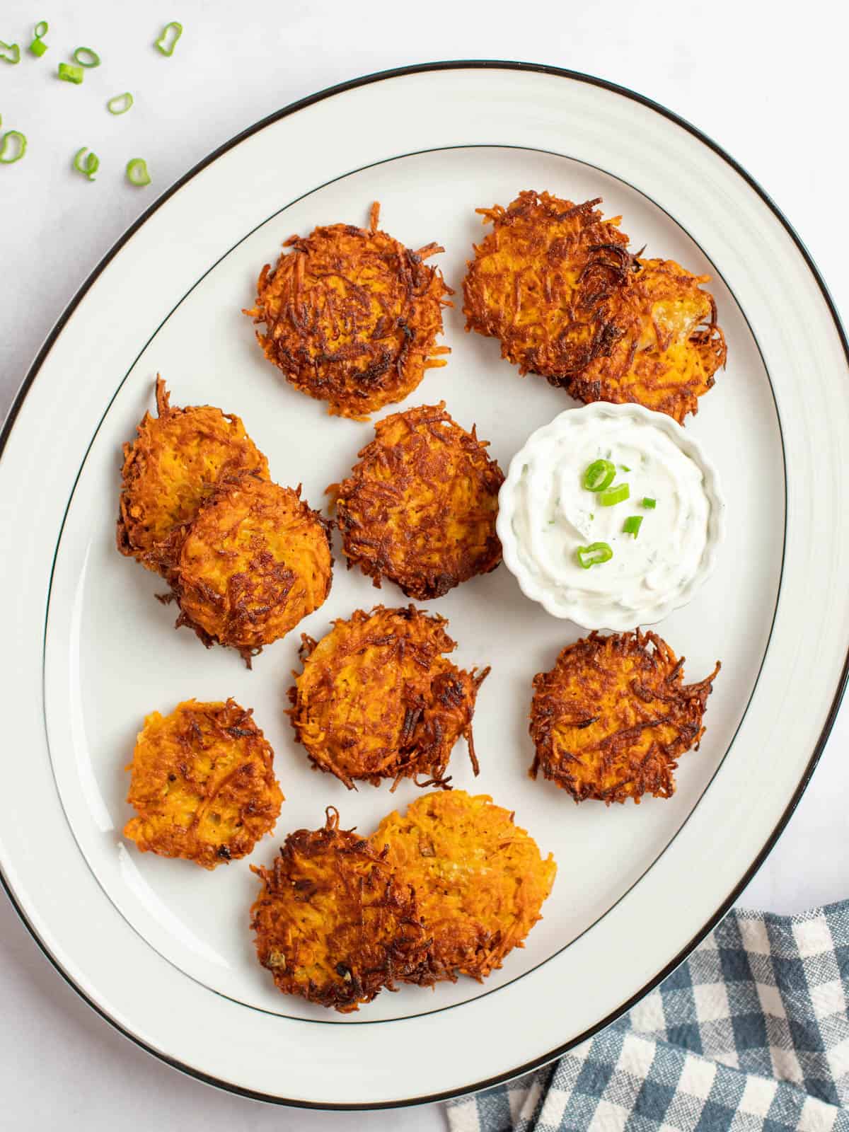 Crispy sweet potato latkes on a plate topped with a side of sour cream.