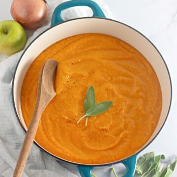 Butternut squash soup in a pot topped with fresh sage and a wooden spoon.