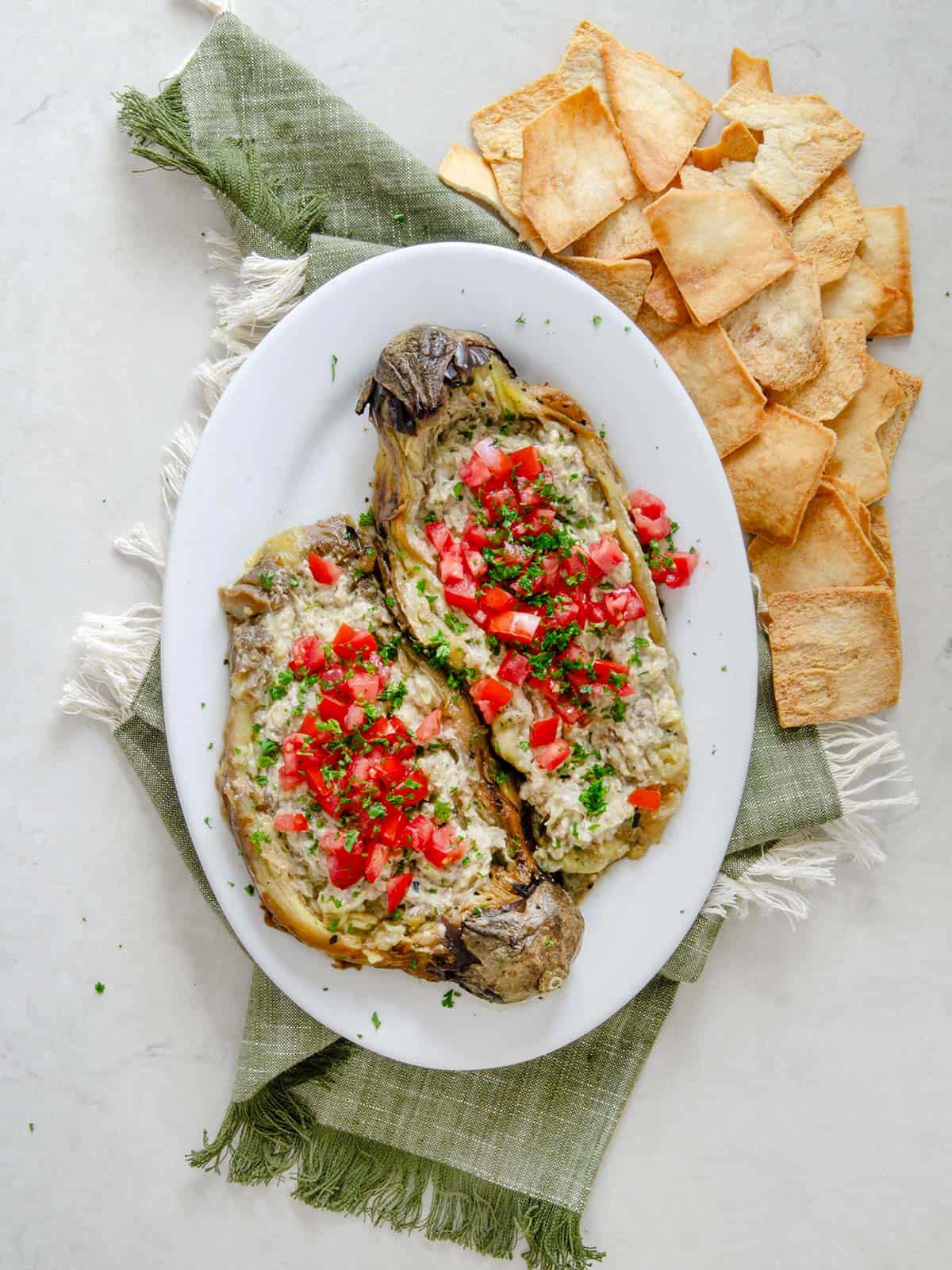 Eggplant dip topped with diced tomatoes and parsley with a side of crackers.