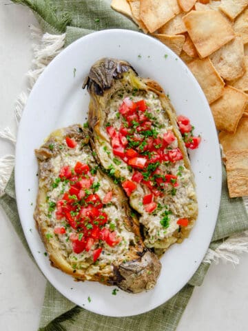 Eggplant dip on a plate topped with diced tomatoes and parsley.