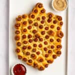 Mini hot dogs in a blanket shaped into a dreidel with ketchup and mustard sides.