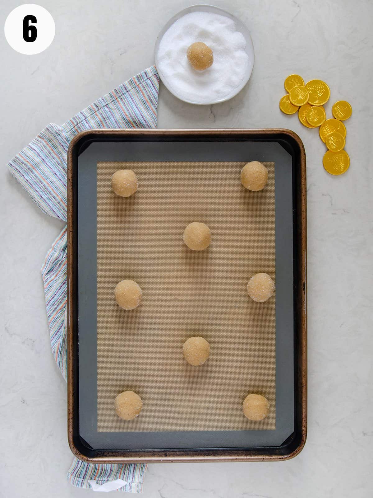 Cookie dough balls rolled in sugar on a baking sheet.
