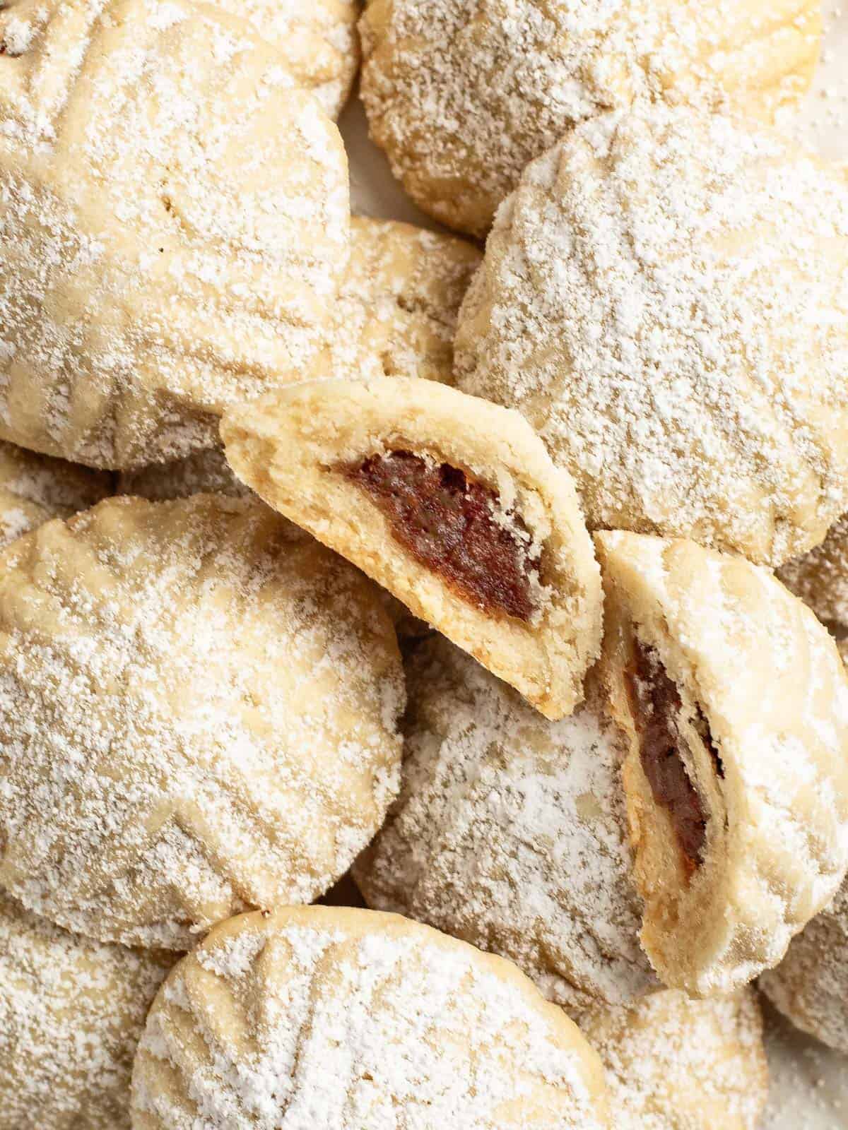 Maamoul cookies topped with powdered sugar and some showing their date filling.