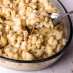 A spoon scooping white cheddar mad and cheese out of a bowl.