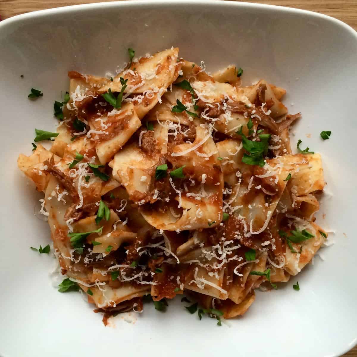 Short rib ragu with pappardelle pasta in a bowl topped with herbs.