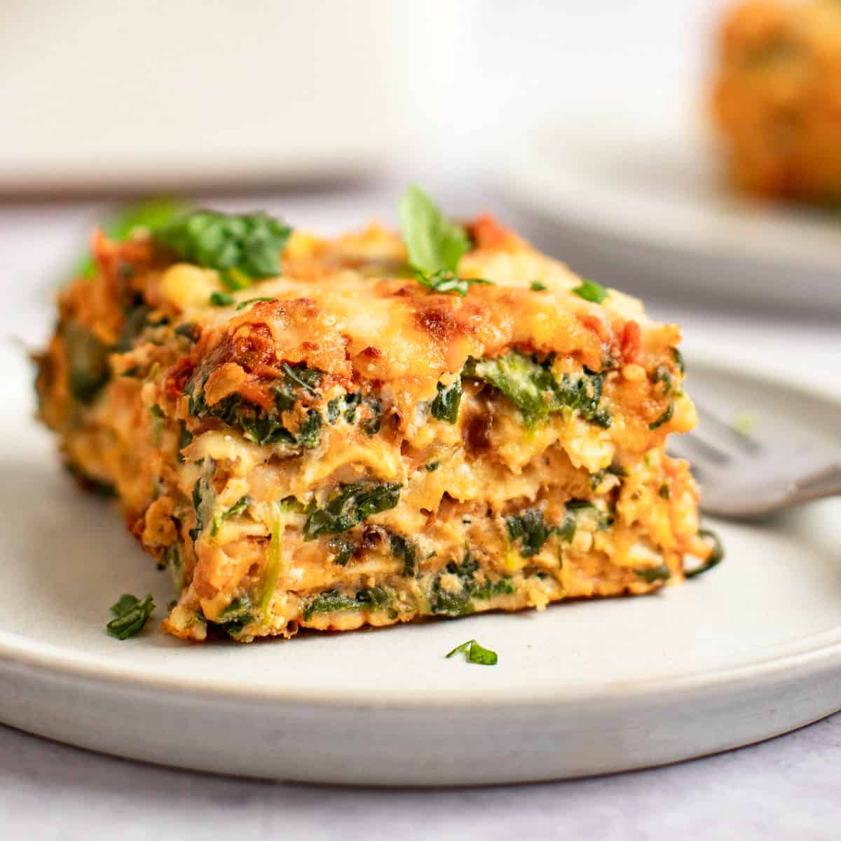 A slice of matzo spinach lasagna topped with fresh basil on a plate.