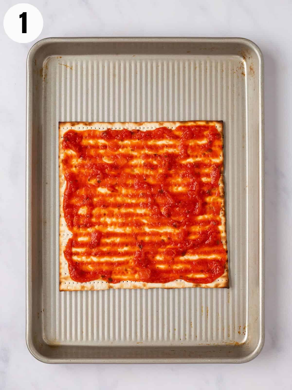 Matzo on a baking sheet topped with marinara sauce.