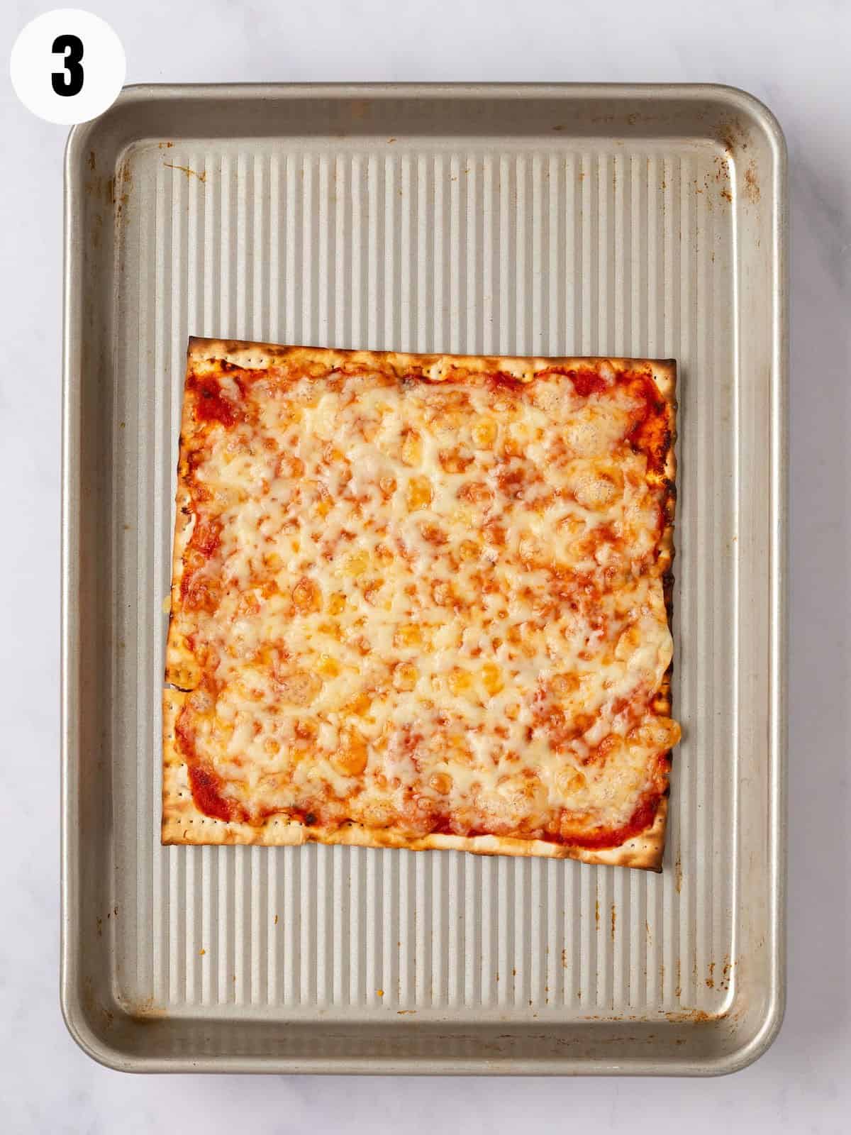 Baked matzo pizza with melted cheese on a baking sheet.