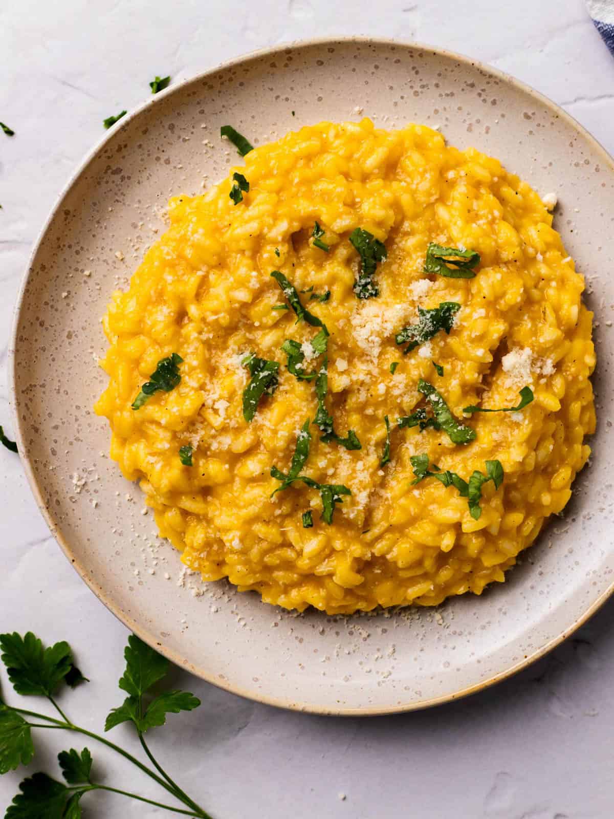 Creamy pumpkin risotto in a bowl topped with parmesan and fresh herbs.