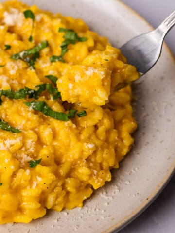 Creamy pumpkin risotto in a bowl topped with parmesan.