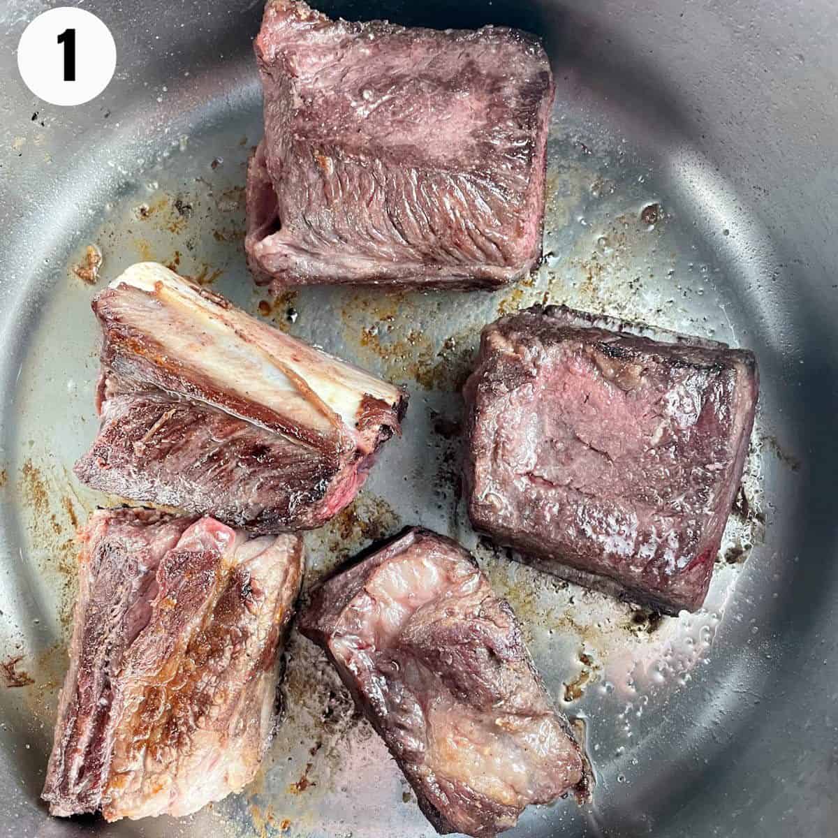 Beef short ribs being seared in a pan until browned.