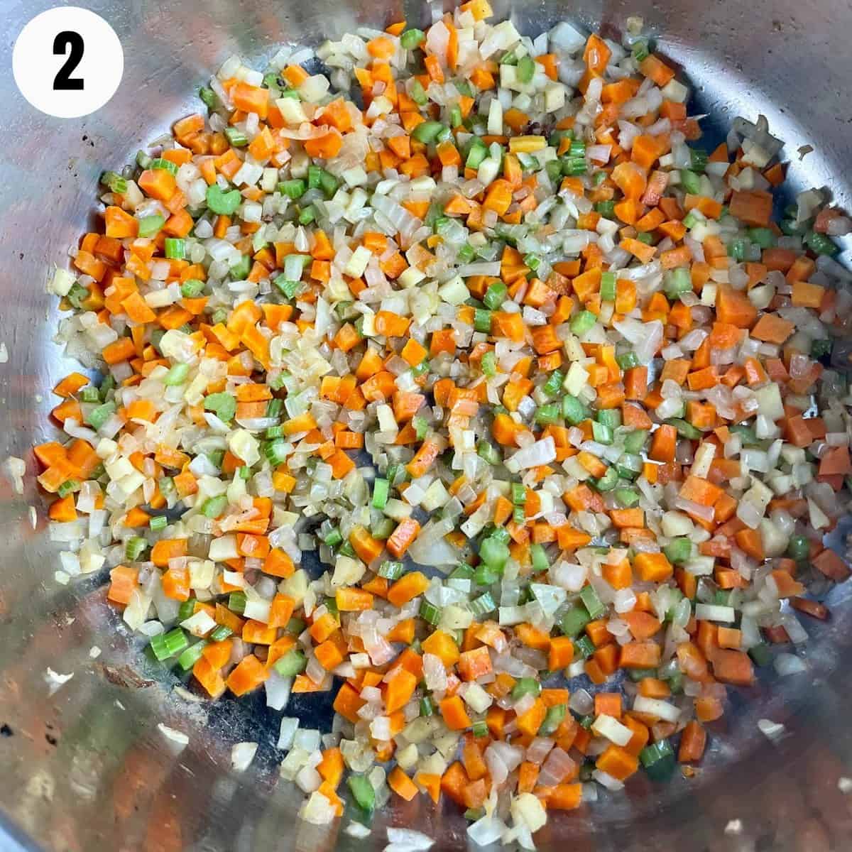 Diced carrots, onion, and celery, being sautéed in a pan.