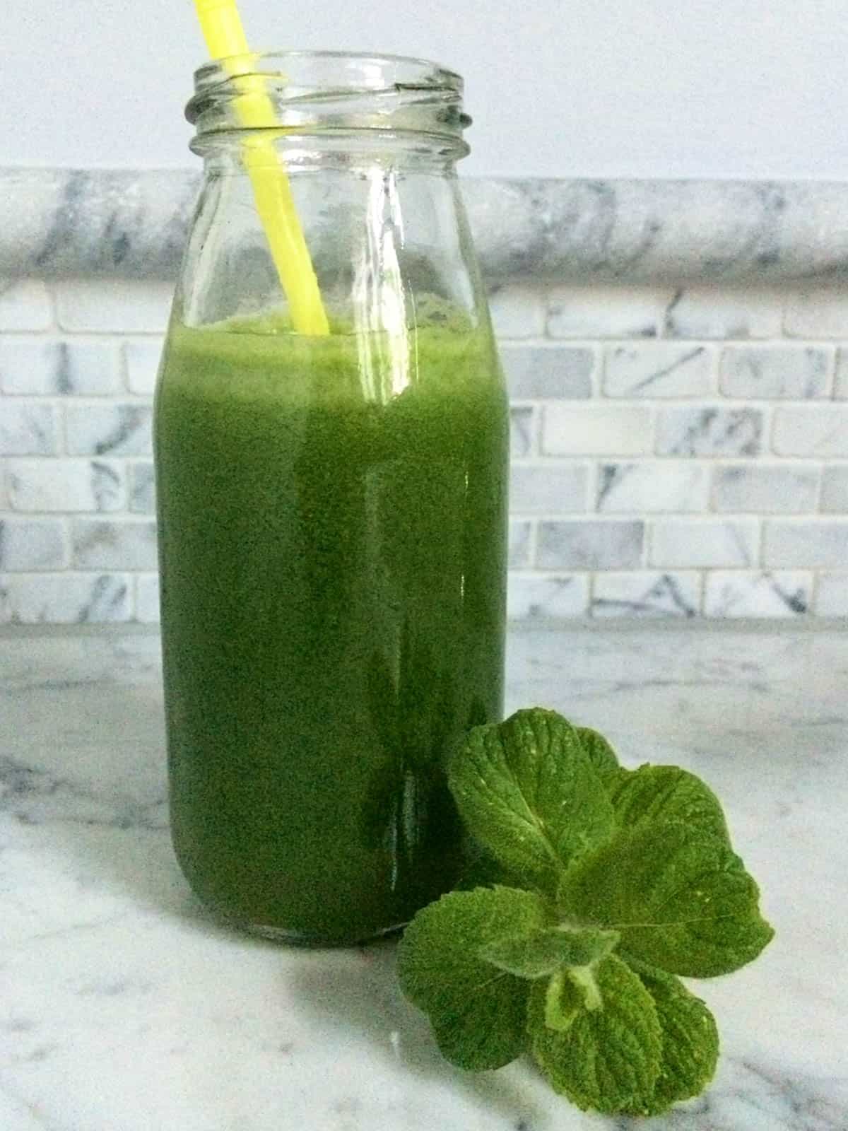 Bottle of green juice with yellow straw and mint sprig.